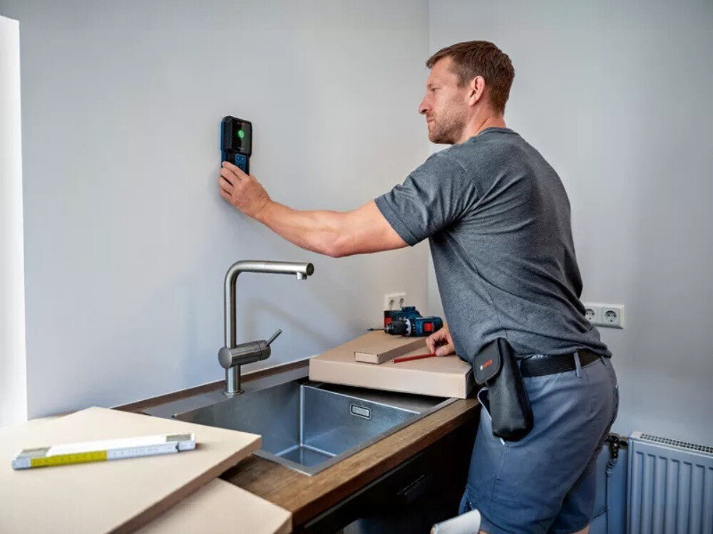 Detektor BOSCH GMS 100-23, wykrywanie, ściana, bezpieczeństwo, pomiar, mężczyzna przykłada detektor do ściany w kuchni nad zlewem
