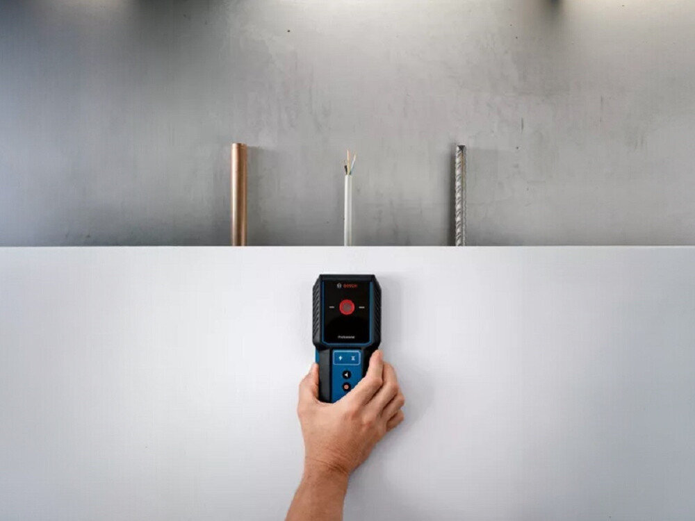 Detektor BOSCH GMS 100-23, detekcja, metal, kable, remont, ręka przykłada detektor do ściany, wizualizacja wykrywania typów obiektów w ścianie