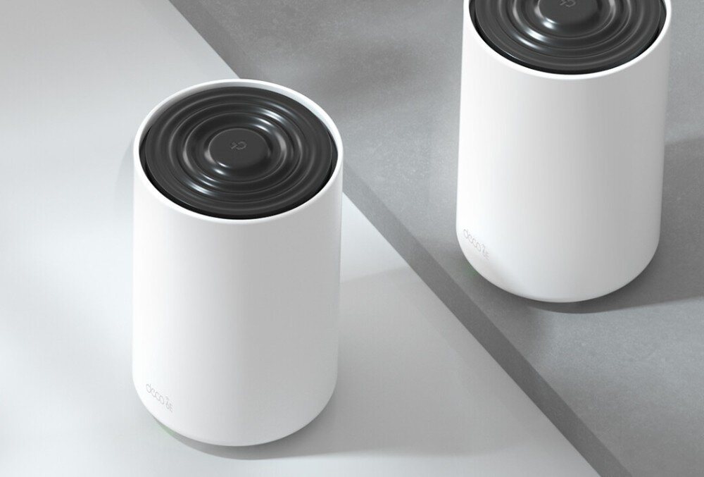 Router TP-LINK Deco XE75 Pro Dwa cylindryczne urządzenia w białej obudowie z czarnym, okrągłym panelem górnym stojące na jasnej powierzchni, opis