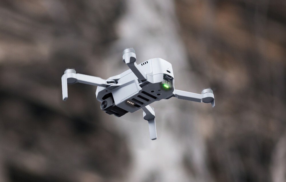 Akumulator POTENSIC do Atom 4K Biały dron z rozłożonymi ramionami uchwycony w locie nad błękitną powierzchnią wody z rozmytym wybrzeżem w tle