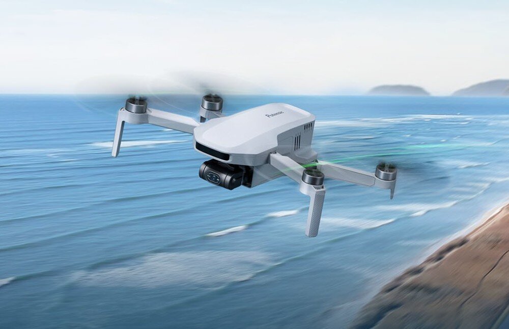 Akumulator POTENSIC do Atom 4K Biały dron z rozłożonymi ramionami uchwycony w locie nad błękitną powierzchnią wody z rozmytym wybrzeżem w tle