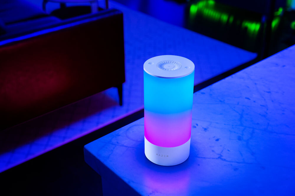 Lampa RAZER Aether Smart Lamp Pro Regulacja jasności, Wi-Fi, Bluetooth prezentacja lampy na stoliku na tle pokoju z oświetleniem ledowym Razer Aether Pro wyjątkowa atmosfera personalizacja kolorów i efektów technologia Razer Chroma RGB aplikacja sterowanie światłem zmiana jasności gotowe sceny harmonogramy bez kabli dopasowanie oświetlenia