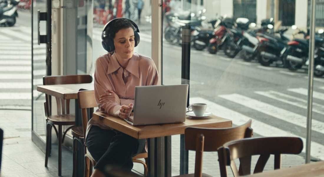 Laptop HP EliteBook 860 - Kobieta nosząca słuchawki siedzi przy biurku z laptopem HP EliteBook 860, koncentrując się na zadaniach.