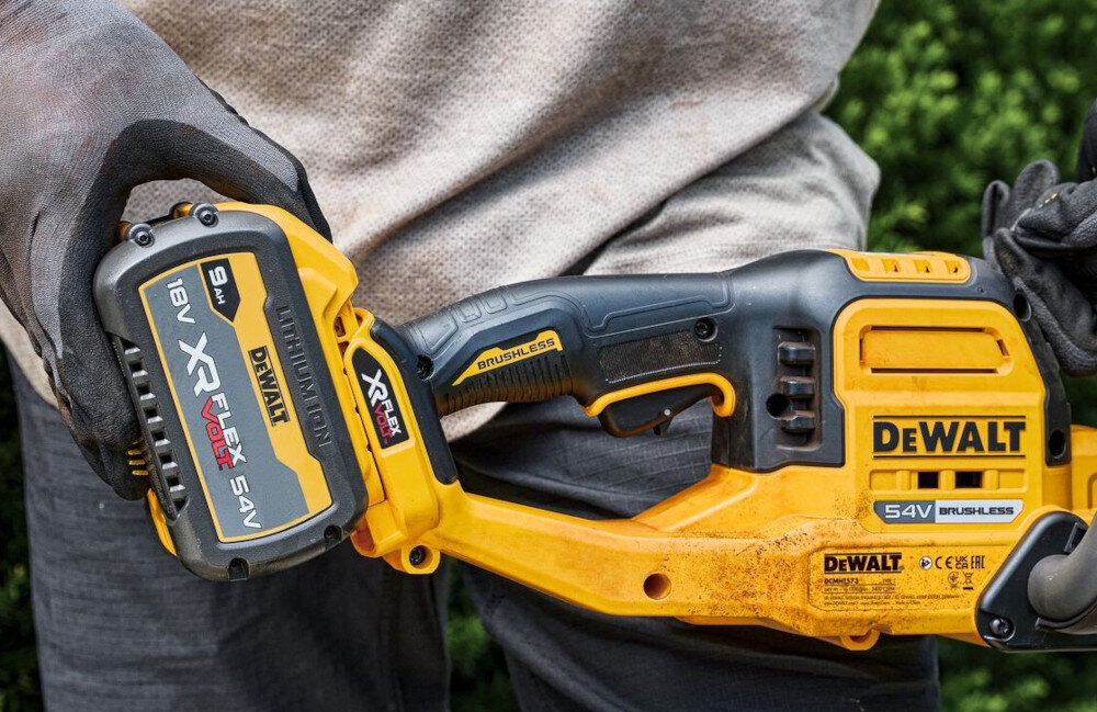 Nożyce do żywopłotu DEWALT DCMHT573N-XJ 650mm 54V akumulatorowe ogród osoba trzyma w dłoniach nożyce wkłada akumulator na miejsce należą do systemu DEWALT XR FlexVolt 54V wygoda pracy bez przewodu parametry zbliżone do narzędzi sieciowych oszczędność czasu i pieniędzy jeden akumulator można wykorzystać w innych narzędziach