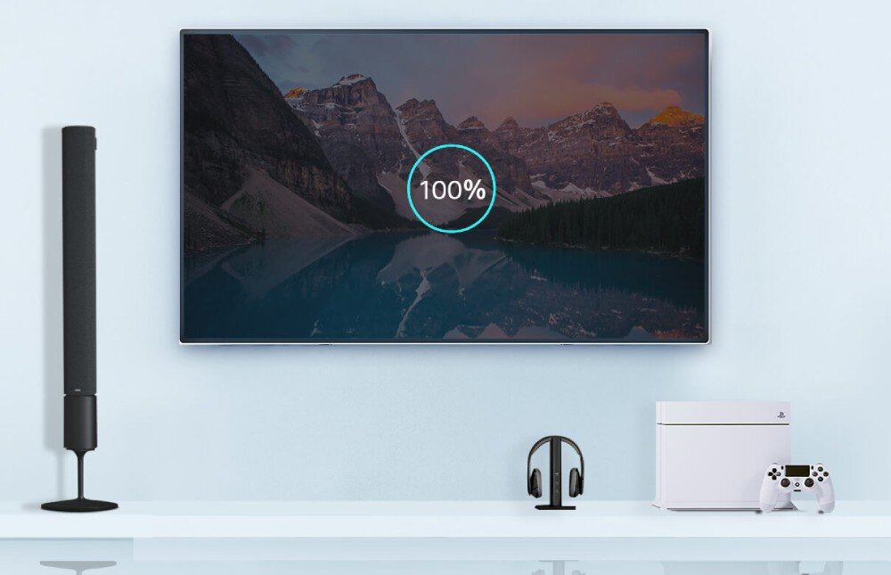 Router TP-LINK Archer AXE75 Ściana z dużym telewizorem wyświetlającym obraz gór i jeziora oraz ikoną wskazującą postęp ładowania 100%. Pod telewizorem stoją głośnik, słuchawki bezprzewodowe oraz konsola do gier, łączność, sieć Wi-Fi, przepustowość