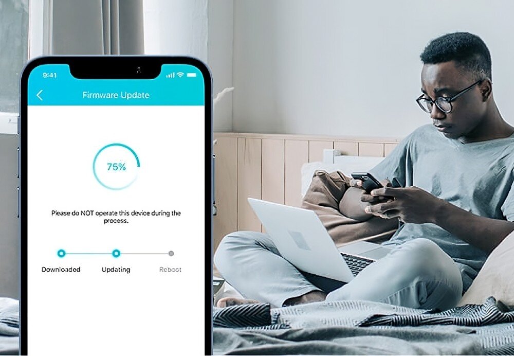 Router TP-LINK Archer AXE75 Widok aplikacji na smartfonie przedstawiającej proces aktualizacji oprogramowania (75%). W tle znajduje się mężczyzna siedzący na łóżku, korzystający z telefonu oraz laptopa, aktualizacja, komendy głosowe, kompatybilność z Amazon Alexa