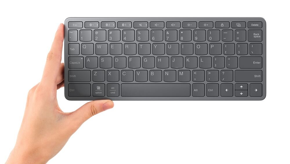 Osoba trzyma czarną klawiaturę z układem QWERTY, posiadającą klawisze funkcyjne i strzałki kierunkowe.