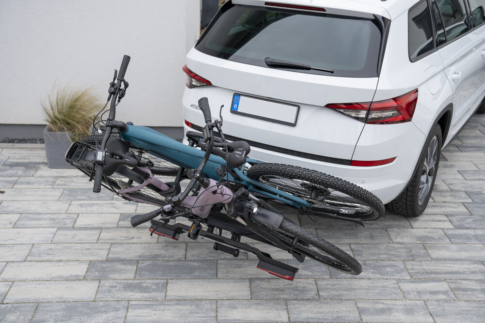 Bagażnik rowerowy FISCHER Roadline na hak 2 rowery Czarny podjazd przed domem bagażnik przymocowany do białego samochodu na bagażniku dwa rowery do rowerów z ramą o maksymalnej średnicy 60 mm kołami w rozmiarze od 12 do 29 cali rozstaw osi wynosi 130 cm odległość między szynami około 25 cm do transportu różnych typów jednośladów
