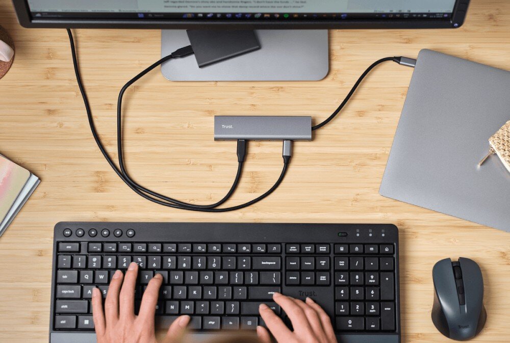 Hub TRUST Halyx 25136 Widok z góry na biurko gdzie szary adapter łączy laptopa z monitorem i dyskiem zewnętrznym obok czarnej klawiatury