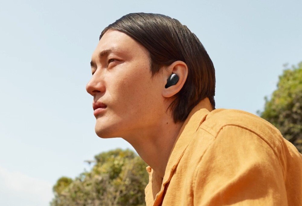 Słuchawki dokanałowe SENNHEISER Accentum True Wireless ANC Mężczyzna z długimi, ciemnymi włosami patrzy przed siebie w słoneczny dzień. W jego uchu znajduje się czarna bezprzewodowa słuchawka, redukcja szumów, ANC, tryb transparentny