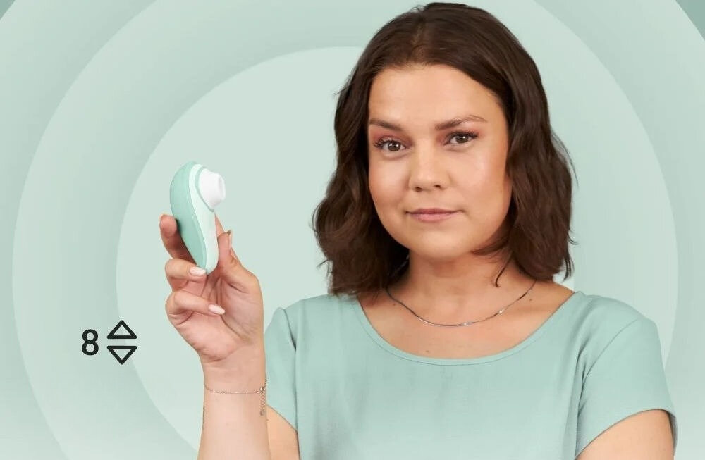 WOMANIZER Liberty 2 Sage bezdotykowy masażer łechtaczki kobieta w zielonej bluzce trzymająca masażer uśmiechnięta 8 poziomów osiem poziomów intensywności dostosowanie doznań subtelna delikatna stymulacja intensywne przeżycia stopniowe przechodzenie między poziomami płynne dopasowanie doświadczeń