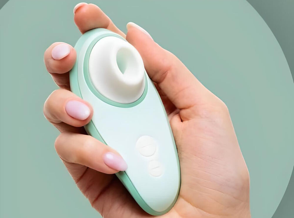 WOMANIZER Liberty 2 Sage bezdotykowy masażer łechtaczki masażer trzymany w ręce zielony ikonka wody przyciski białe elementy elegancja i technologia pełna wodoodporność klasy IPX7 wyjątkowe doznania relaksująca kąpiel w wannie odświeżający prysznic w basenie solidna konstrukcja bezproblemowe działanie pod wodą różne sposoby na przyjemność dla miłośników wodnych przygód