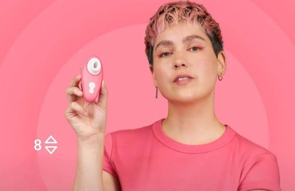 WOMANIZER Liberty 2 Vibrant Rose bezdotykowy masażer łechtaczki kobieta w różowej bluzce trzymająca masażer uśmiechnięta 8 poziomów osiem poziomów intensywności dostosowanie doznań subtelna delikatna stymulacja intensywne przeżycia stopniowe przechodzenie między poziomami płynne dopasowanie doświadczeń