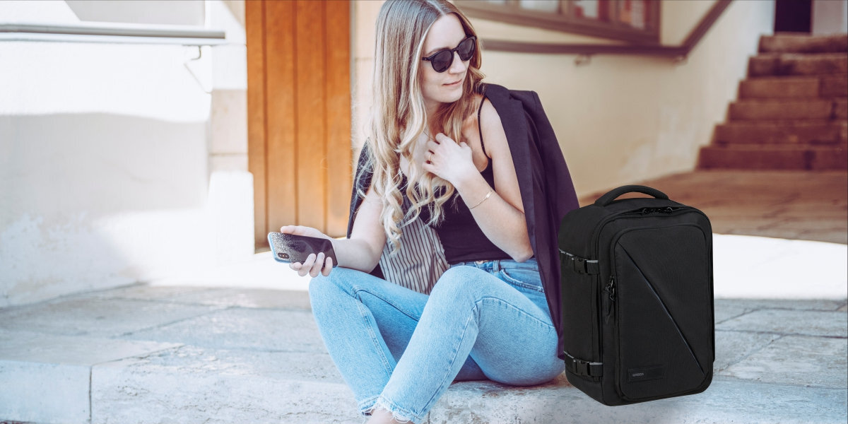 AMERICAN TOURISTER Take2Cabin na zdjęciu widać siędząco na schodkach kobietę, obok niej znjaduje się plecak w kolorze czarnym
