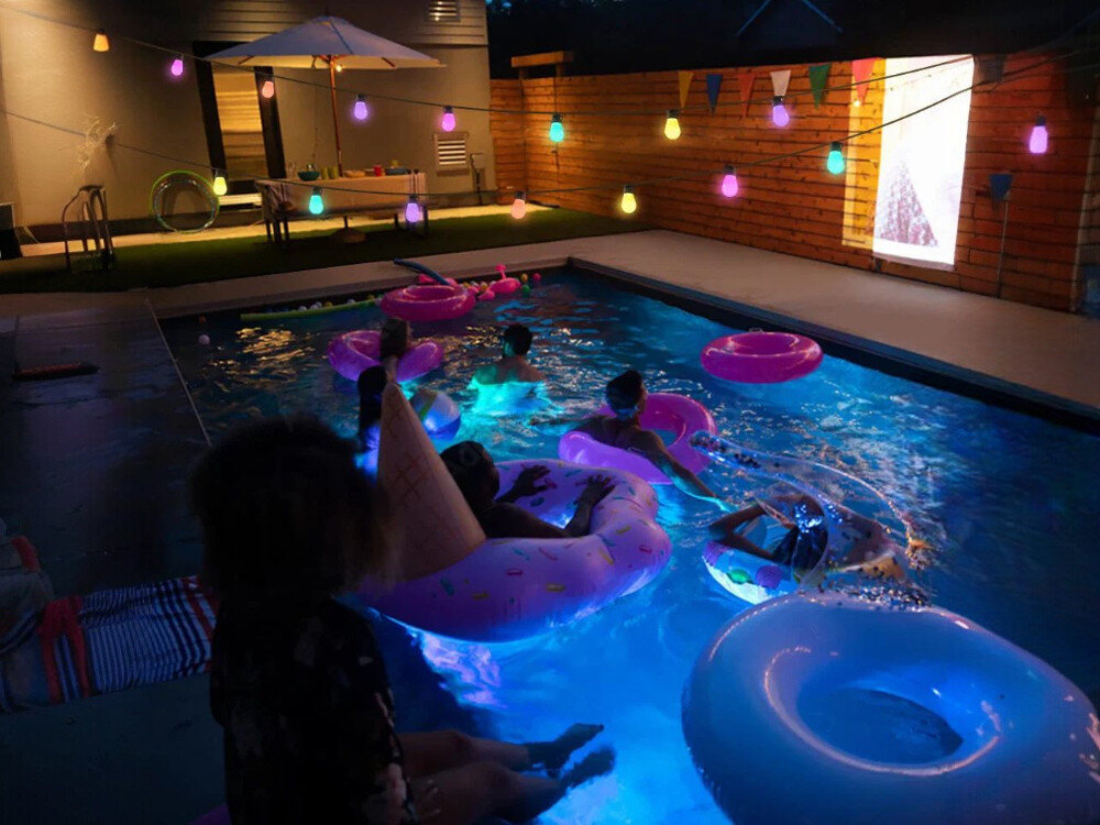 Girlanda ogrodowa GOVEE H7020 RGBW 48FT Outdoor string light Wi-Fi/Bluetooth, sceny, muzyka, DIY, harmonogram, Basen nocą z kolorowym oświetleniem LED i bawiącymi się dziećmi.