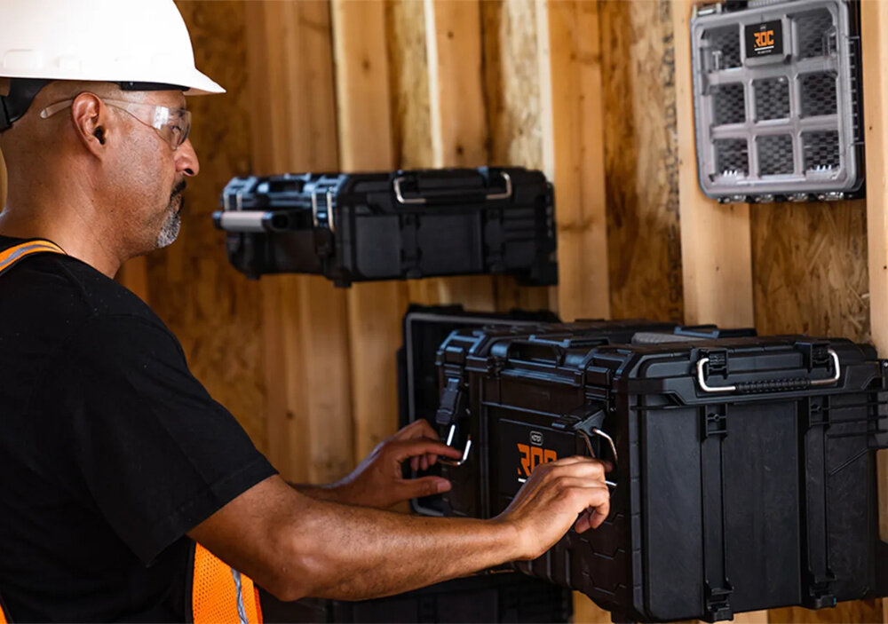 Skrzynka narzędziowa KETER Roc Pro Gear 17211898 pomieszczenie drewniana ściana skrzynka zawieszona na ścianie obok osoba waga około 4,25 kg wymiary 57,1 x 35,1 x 35,6 cm lekka i łatwa w przenoszeniu pojemność do 37,4 l ładowność do 54 kg