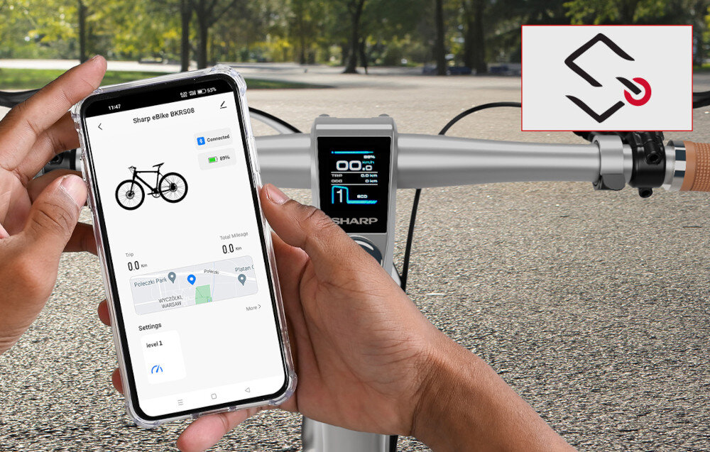 Rower elektryczny SHARP BK-RS08-ES M21 Srebrny park zbliżenie na dłonie osoby osoba trzyma telefon z włączoną aplikacją moduł Bluetooth aplikacja SHARP Life łatwy dostęp do kluczowych informacji pełna kontrola
