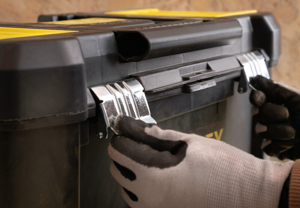 Wózek narzędziowy z organizerem STANLEY STST1-81320 pomieszczenie osoba trzyma zatrzaski w dłoniach metalowe zatrzaski zawiasy z wysokiej jakości tworzywa sztucznego trwałość stabilność zawartość jest lepiej chroniona przed wypadaniem i uszkodzeniem