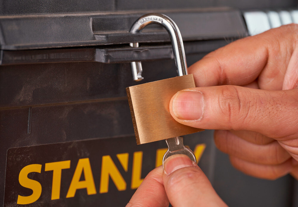 Wózek narzędziowy z organizerem STANLEY STST1-81320 zbliżenie na otwór do montażu kłódki osoba zakłada kłódkę na skrzynkę możliwość zamknięcia na kłódkę bezpieczeństwo przechowywanych narzędzi cenne akcesoria są dobrze chronione