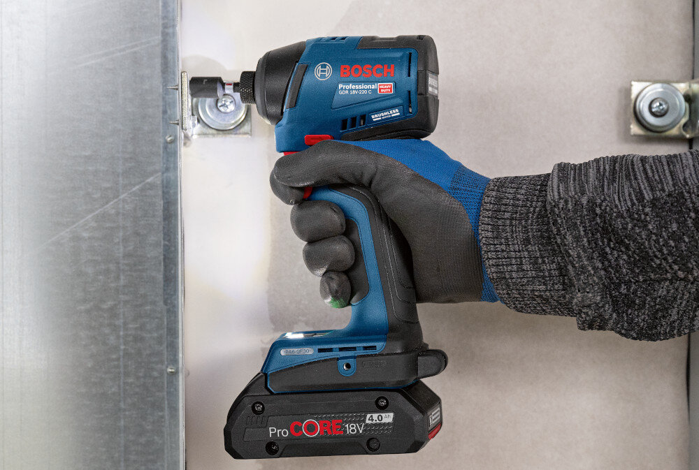 Klucz udarowy BOSCH Professional GDR 18V-220 C 06019L6000 pomieszczenie ściany osoba przykręca zawias do ściany widoczna włączona dioda dwie diody LED doświetlają obszar wkręcania mogą być włączane niezależnie łatwiej ustawić bit w gnieździe uniknąć ześlizgnięcia się końcówki dokładność i bezpieczeństwo