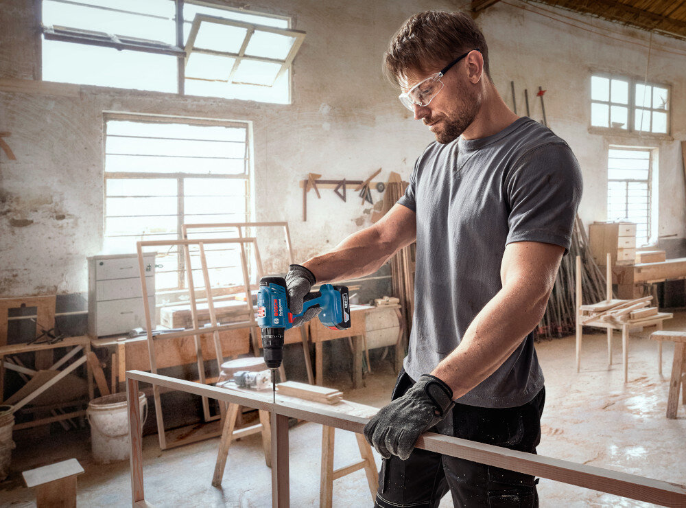 Wiertarko-wkrętarka BOSCH Professional GSB 183-LI 06019K9100 garaż warsztat drewniane elementy osoba używa wiertarko-wkrętarki wyważona konstrukcja pistoletowa masa 1,5 kg z akumulatorem niski poziom wibracji do 1 m/s² przy wierceniu w metalu