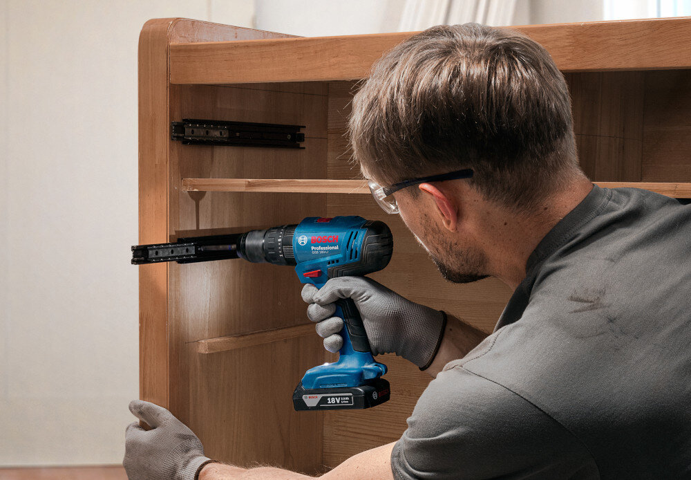 Wiertarko-wkrętarka BOSCH Professional GSB 183-LI 06019K9100 pomieszczenie osoba używa wiertarko-wkrętarki przykręca prowadnice w szafce widoczne oświetlenie wbudowane oświetlenie ułatwia pracę w słabo oświetlonych miejscach i redukuje błędy