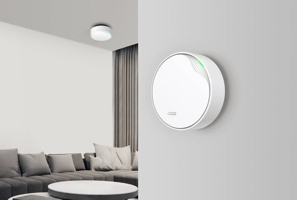 Router TP-LINK Deco X50-PoE Białe, okrągłe urządzenie zamontowane na ścianie w nowoczesnym salonie. W tle widać sofę, stolik i zasłony. Pod sufitem znajduje się drugie identyczne urządzenie, opis