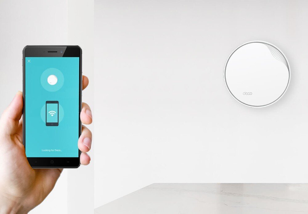 Router TP-LINK Deco X50-PoE Osoba trzyma smartfon z otwartą aplikacją do konfiguracji urządzenia. W tle na ścianie znajduje się router, aplikacja, narzędzia, komendy głosowe