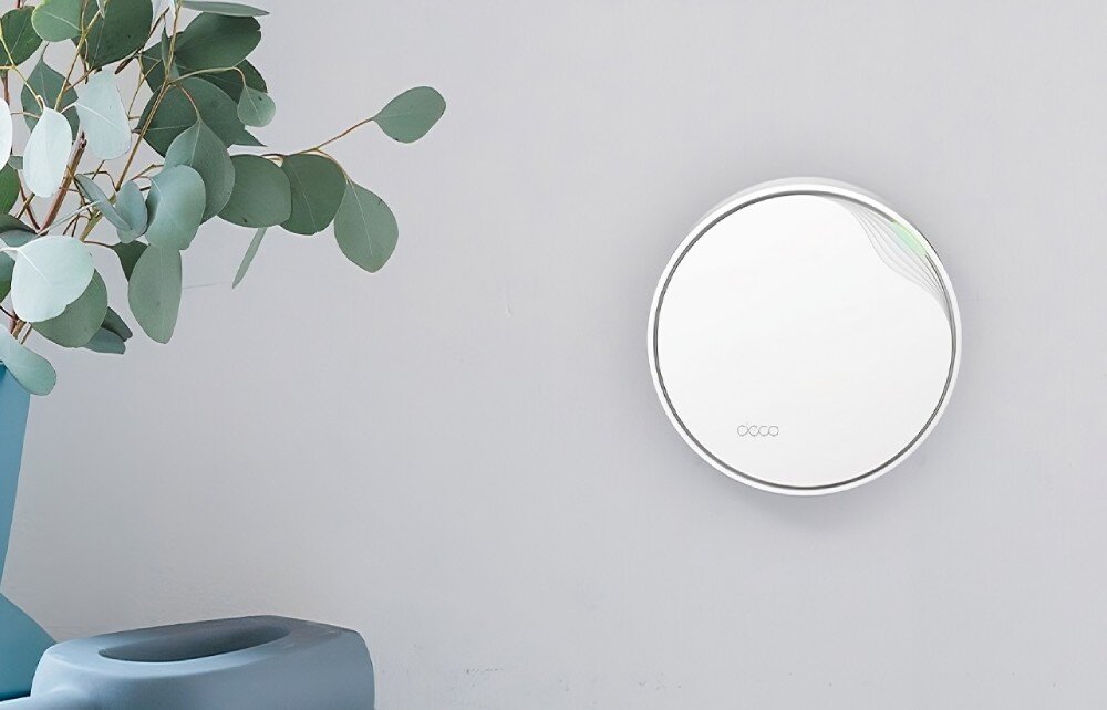 Router TP-LINK Deco X50-PoE Białe, okrągłe urządzenie zamontowane na jasnej ścianie, obok niebieskiej doniczki z rośliną o zielonych liściach, wielkość, wygląd, wymiary