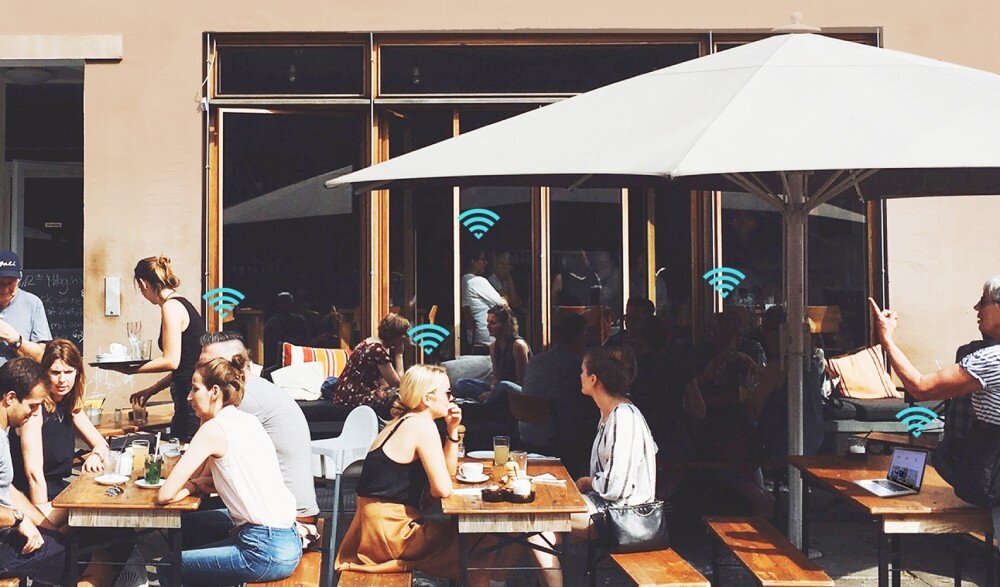 Router TP-LINK TL-MR105 Zewnętrzna kawiarnia z ludźmi siedzącymi przy drewnianych stołach. Nad ich głowami widoczne ikony sygnału Wi-Fi, sieć Wi-Fi, pasmo 2,4 GHz, prędkość