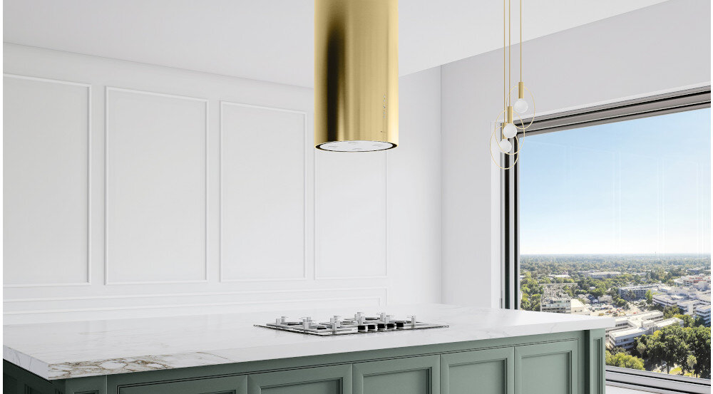 OKAP GLOBALO CYLINDRO ISOLA 39.7 Złoty mat Zdjęcie przedstawia kuchnię z wyspą wyposażoną w płytę grzewczą. Nad wyspą zamontowany jest okap w kształcie złotej tuby z czterema wbudowanymi lampkami LED. W centralnym miejscu na wyspie stoi roślina w doniczce, a w tle widać eleganckie, połyskujące szafki oraz detale kuchenne. Całość utrzymana jest w jasnej, minimalistycznej aranżacji z kontrastowym złotym akcentem wyspowy globalo złoty mat stal szlachetna tuba kuchenny sufitowy design premium wyspa cylindryczny elegancki kuchnia agd wydajny dekoracyjny