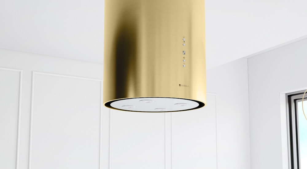 OKAP GLOBALO CYLINDRO ISOLA 39.7 Złoty mat Zdjęcie przedstawia detal okapu w kształcie złotej tuby, zawieszonego nad wyspą kuchenną. W tle widoczna jest jasna ściana z pionowymi drewnianymi listwami i cztery obrazy w ramkach. Poniżej częściowo widać drewniany stół z krzesłami oraz elementy blatu kuchennego z doniczką. Kompozycja podkreśla elegancki design oraz wykończenie wnętrza czyste powietrze wydajność 742 m3/h usuwanie pary tłuszczu zapachów tryb wyciąg tryb pochłaniacz filtr aluminiowy filtr węglowy wentylacja świeżość kuchnia okap skuteczny