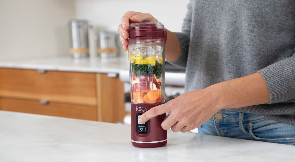Ninja BC151EUCR blender przenośny blender czerwona obudowa składniki wewnątrz pojemnika osoba naciska przycisk łatwość obsługi funkcja pulsowanie i blendowania jeden przycisk przykręcenie kielicha do podstawy załadować składniki założenie pokrywy włączenie urządzenia naciśnięcie przycisku START/STOP blendowanie przez 30 sekund po zakończeniu obrócenie blendera zdjęcie podstawki silnika