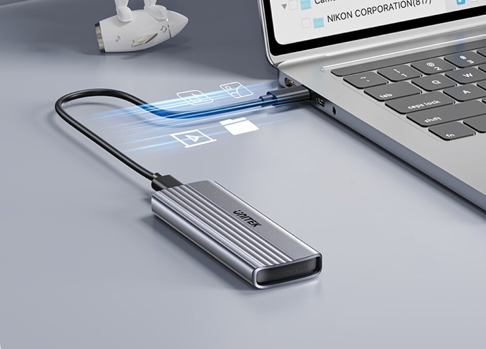 Obudowa dysku UNITEK S1241B01 Srebrna obudowa na dysk podłączona czarnym kablem do bocznego portu laptopa, z widocznymi niebieskimi liniami symbolizującymi przesył danych oraz ikonami folderu, wideo i zdjęć na szarym blacie