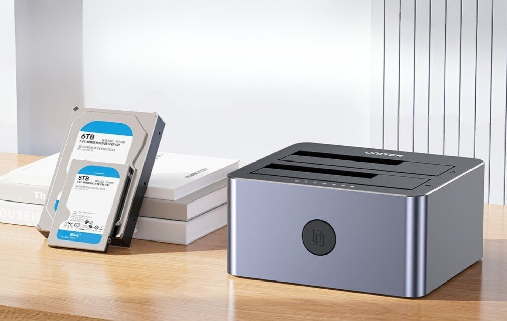 Stacja dokująca UNITEK Y-3027GY01-EU Pusta stacja dokująca stojąca na drewnianym blacie obok dwóch dysków twardych opartych o stos książek