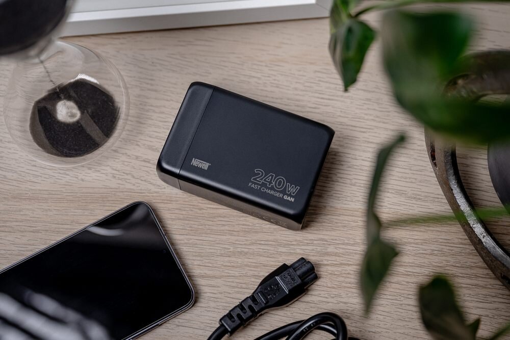 Ładowarka Newell GaN 240 W leży na stole obok telefon