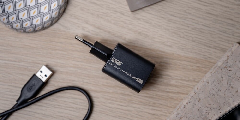 Ładowarka Newell GaN 33 W leżąca na blacie, obok widoczny kabel