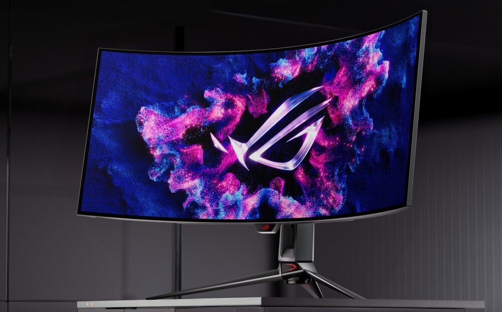 Monitor ASUS ROG Swift PG39WCDM Zakrzywiony monitor gamingowy z podświetlonym logo na ekranie, otoczonym efektownymi różowo-niebieskimi wzorami. Urządzenie stoi na biurku w ciemnym pomieszczeniu, opis
