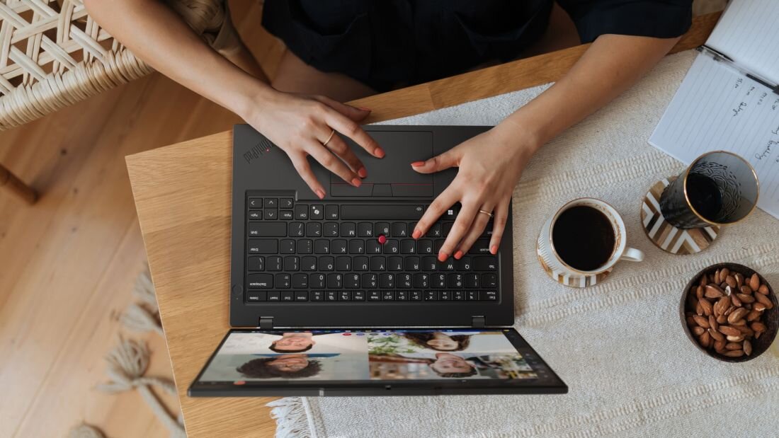 Ręce kobiety piszącej na klawiaturze laptopa Lenovo ThinkPad z wideokonferencją na ekranie i kawą na stole.  - Podświetlana klawiatura Czytnik linii papilarnych 