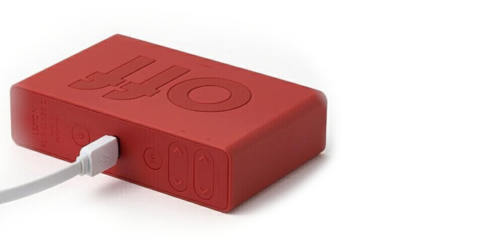 Budzik LEXON Flip Classic Czerwony, akumulator, USB-C, trwałość, użyteczność, Zbliżenie na czerwony budzik w silikonowej obudowie, podłączony do ładowarki USB, widoczne przyciski z boku.