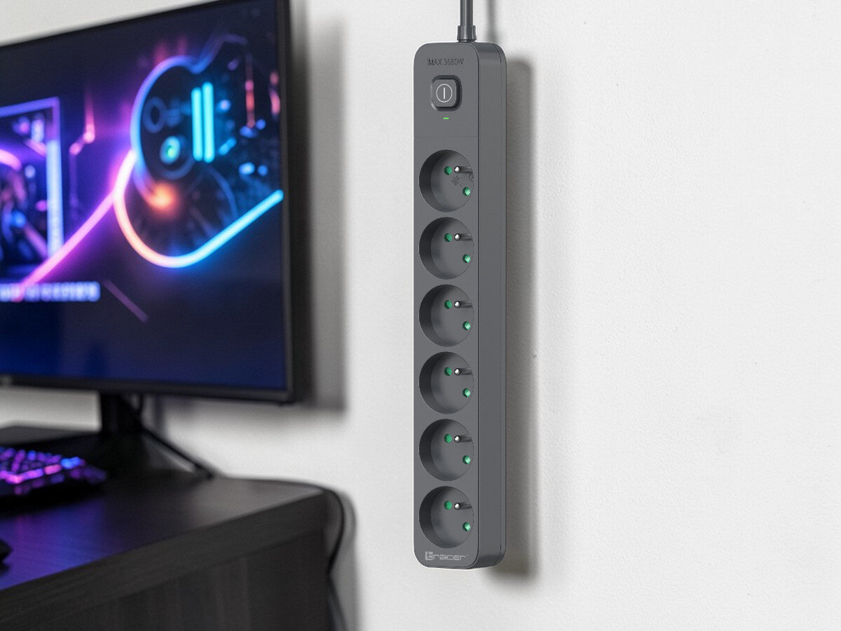 Na ścianie wisi grafitowa listwa zasilająca z sześcioma gniazdami i podświetlanym przyciskiem. Obok znajduje się monitor z kolorową grafiką na ekranie.