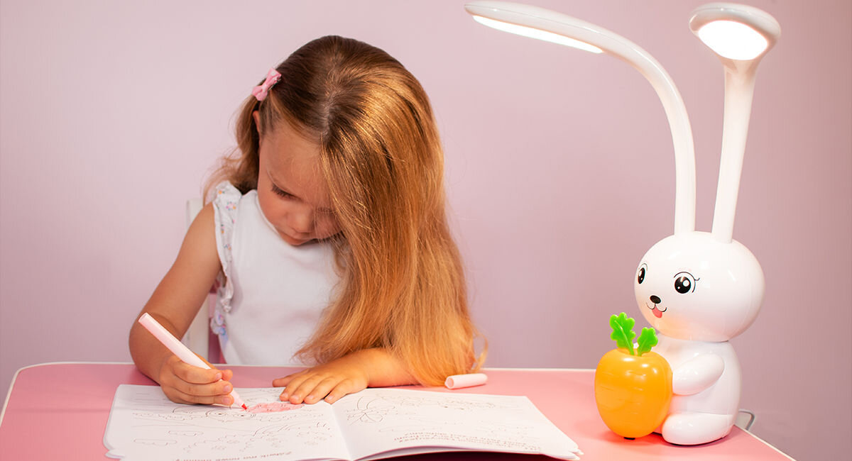 Lampka nocna LED MAXCOM Charlie ML4910 Biały, oszczędności, prąd, rachunki, Dziewczynka pisze w zeszycie, obok lampka świeci i oświetla biurko