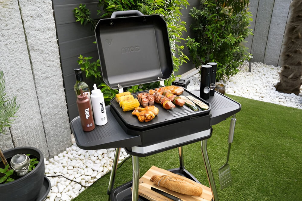 Grill elektryczny UNOLD 58585 Jimmy stojący grill otwarty wewnątrz potrawy obok na półce sosy trawa drzewka Bezpieczeństwo pełna ochrona funkcja zabezpieczenia przed przegrzaniem osłona chroniąca przed wiatrem i zachlapaniem ustawienie pionowe łatwe ściągnięcie do czyszczenia odporność na rozpryskującą się wodę (IPX4) na świeżym powietrzu