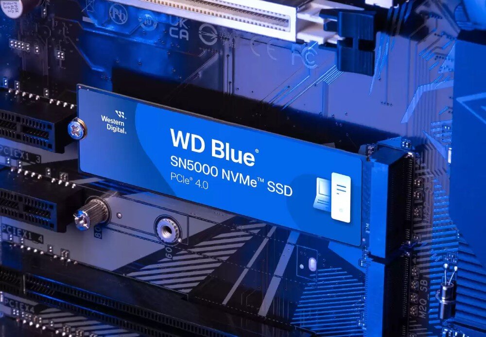 Dysk SANDISK WD Blue SN5000 Zbliżenie na wnętrze komputera, gdzie w gnieździe na płycie głównej umieszczono dysk z niebieską naklejką z napisem 'WD Blue' w niebieskiej poświacie