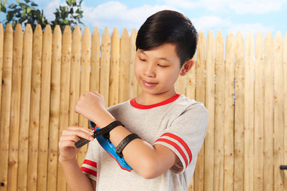 Wyrzutnia HASBRO Marvel Spider-Man Rel Webs F87345L0 Prezentacja mechanizmu przeładowania wyrzutni Nerf Elite 2.0. Dłoń dziecka odciąga do tyłu czarny uchwyt znajdujący się pod celownikiem. Wyrzutnia jest załadowana czterema strzałkami gotowymi do wystrzału.