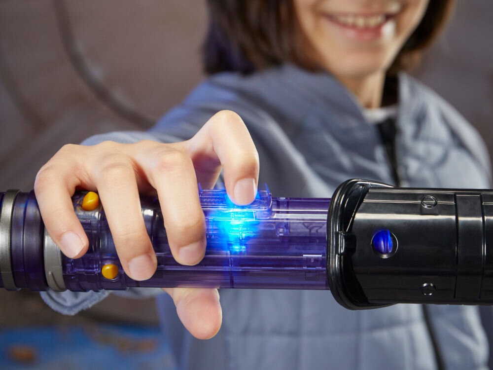 Osoba trzyma miecz świetlny z niebieskim podświetleniem na rękojeści. Miecz ma czarną i przezroczystą konstrukcję z widocznymi żółtymi przyciskami.