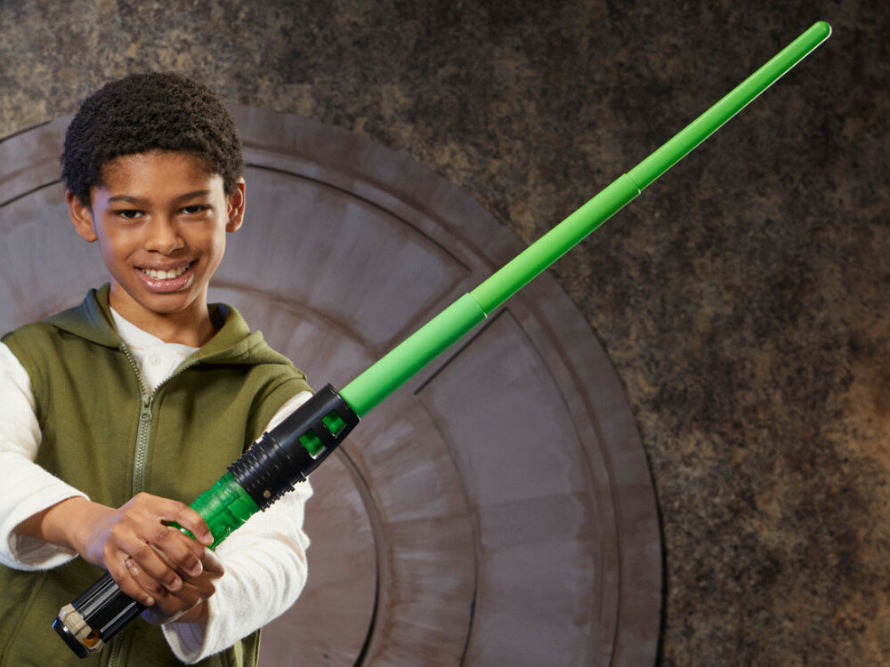Miecz świetlny HASBRO Star Wars Luke Skywalker F99685X0 Uśmiechnięty chłopiec trzymający oburącz zielony miecz świetlny Star Wars Forge. Zabawka jest w pełni rozłożona i gotowa do zabawy.