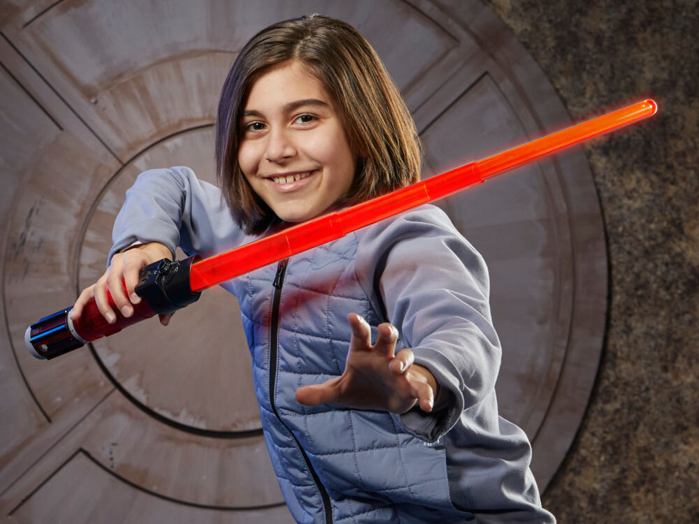 Osoba trzymająca czerwony miecz świetlny na tle futurystycznej ściany. Miecz ma czarną rękojeść z czerwonymi elementami.