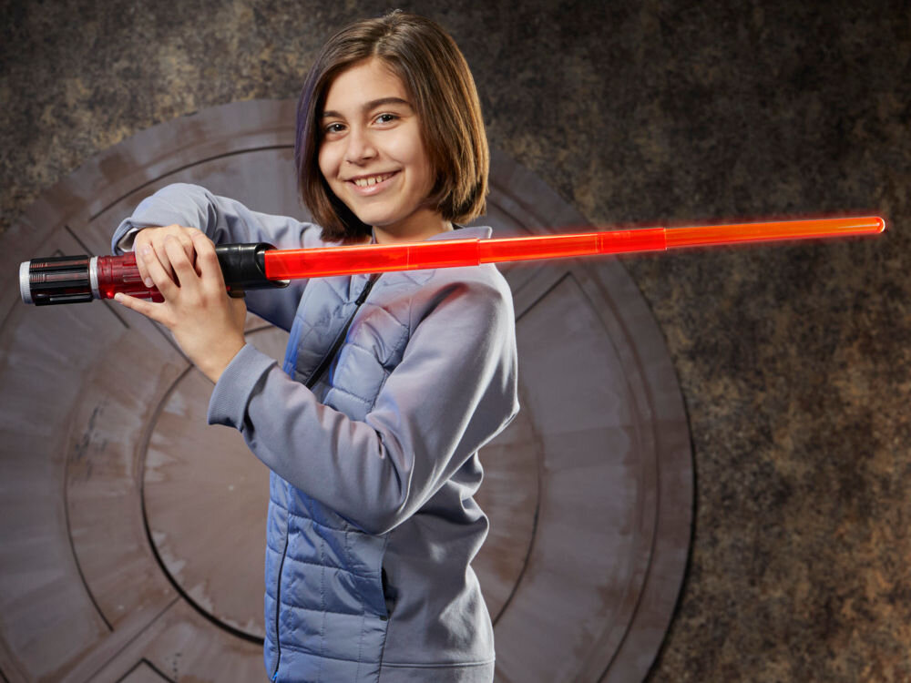 Osoba trzymająca czerwony miecz świetlny na tle futurystycznej ściany. Miecz ma czarną rękojeść z czerwonymi elementami.