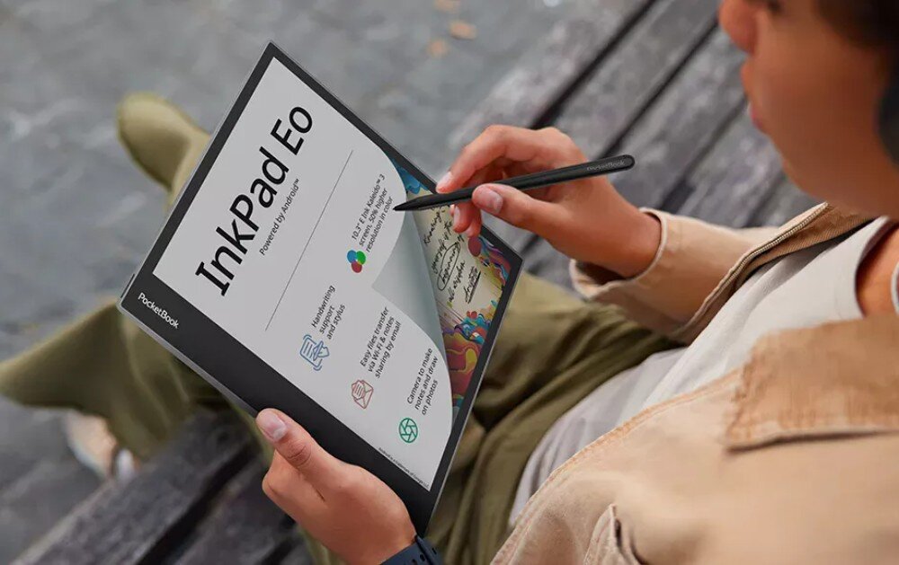 Czytnik e-booków POCKETBOOK InkPad Eo Młoda osoba siedzi na ławce i trzyma w dłoni czytnik z rysikiem. Na ekranie widoczny jest interfejs z napisem 'InkPad Eo' oraz kolorowa ilustracja i ikony symbolizujące funkcje urządzenia, opis